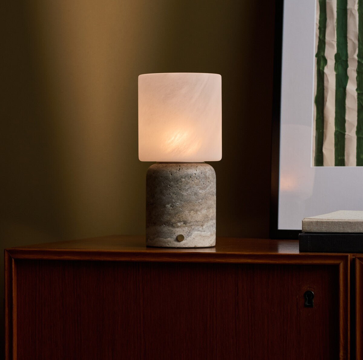 Tavellio Cuyp Large cordless table lamp glowing on a wood cabinet beside stacked books