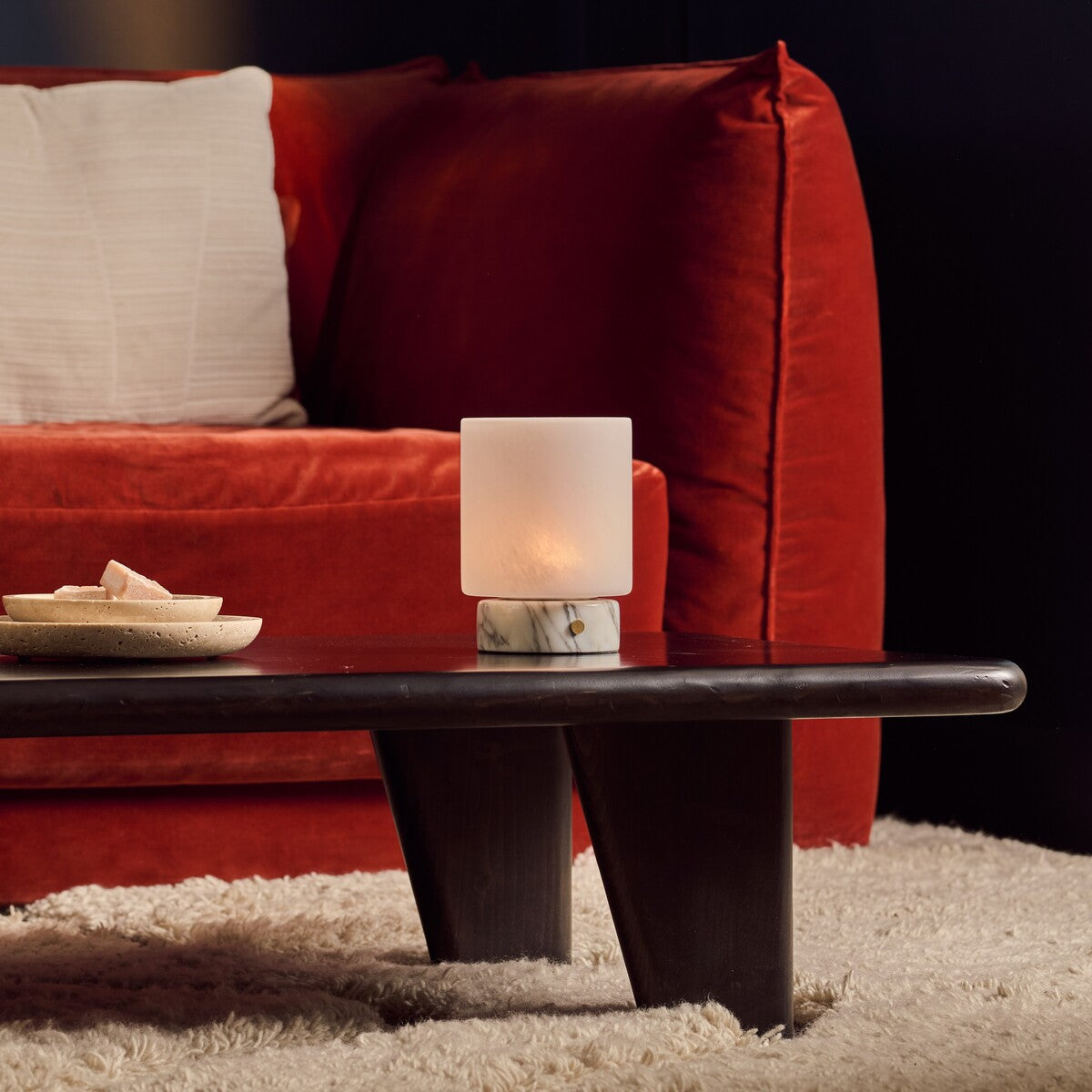 Arabescato marble Cuyp Small rechargeable table lamp on a dark coffee table by a red velvet sofa