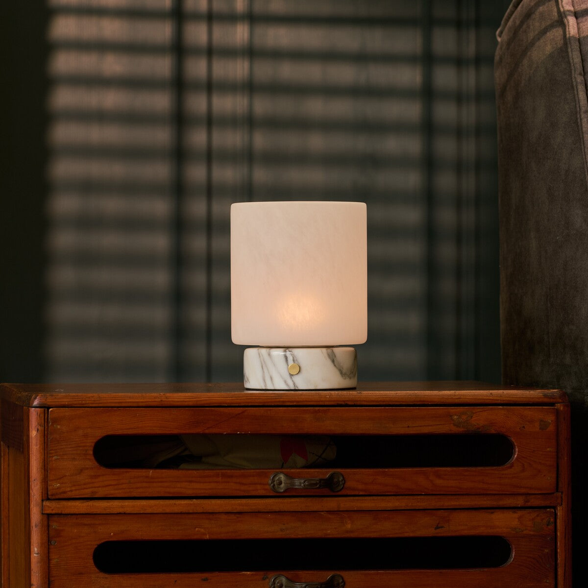 Cordless table lamp with Arabescato marble base glowing on a dark dresser at night