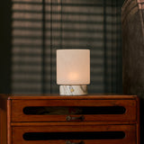 Cordless table lamp with Arabescato marble base glowing on a dark dresser at night