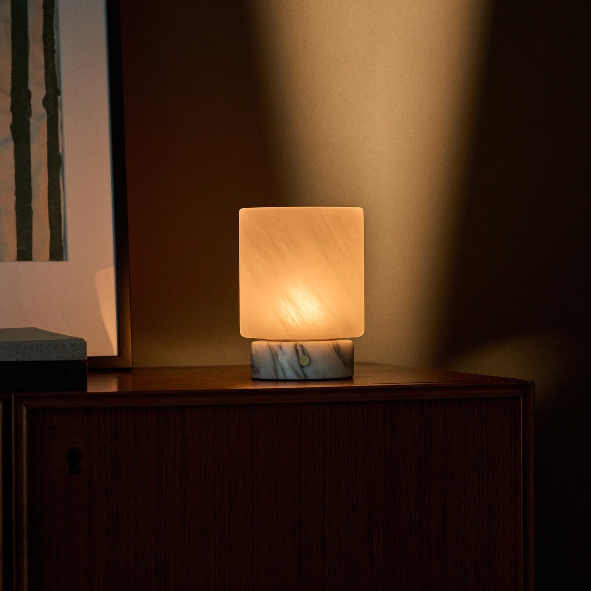 Tavellio Cuyp Small rechargeable table lamp beside a striped green print on a dark wood cabinet