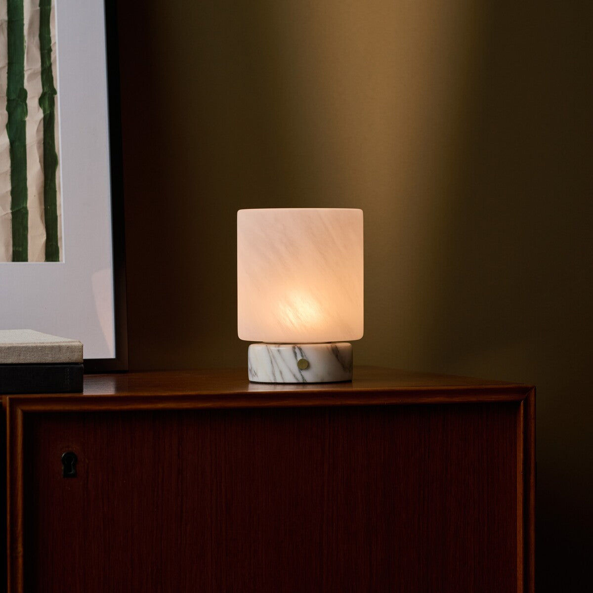 Cordless table lamp with softly veined marble base close up on a dark wood cabinet