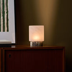 Cordless table lamp Cuyp Small in Calacatta Viola marble glowing on a wood cabinet beside framed art