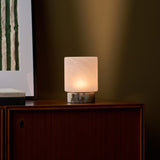 Cordless table lamp Cuyp Small in Calacatta Viola marble glowing on a wood cabinet beside framed art