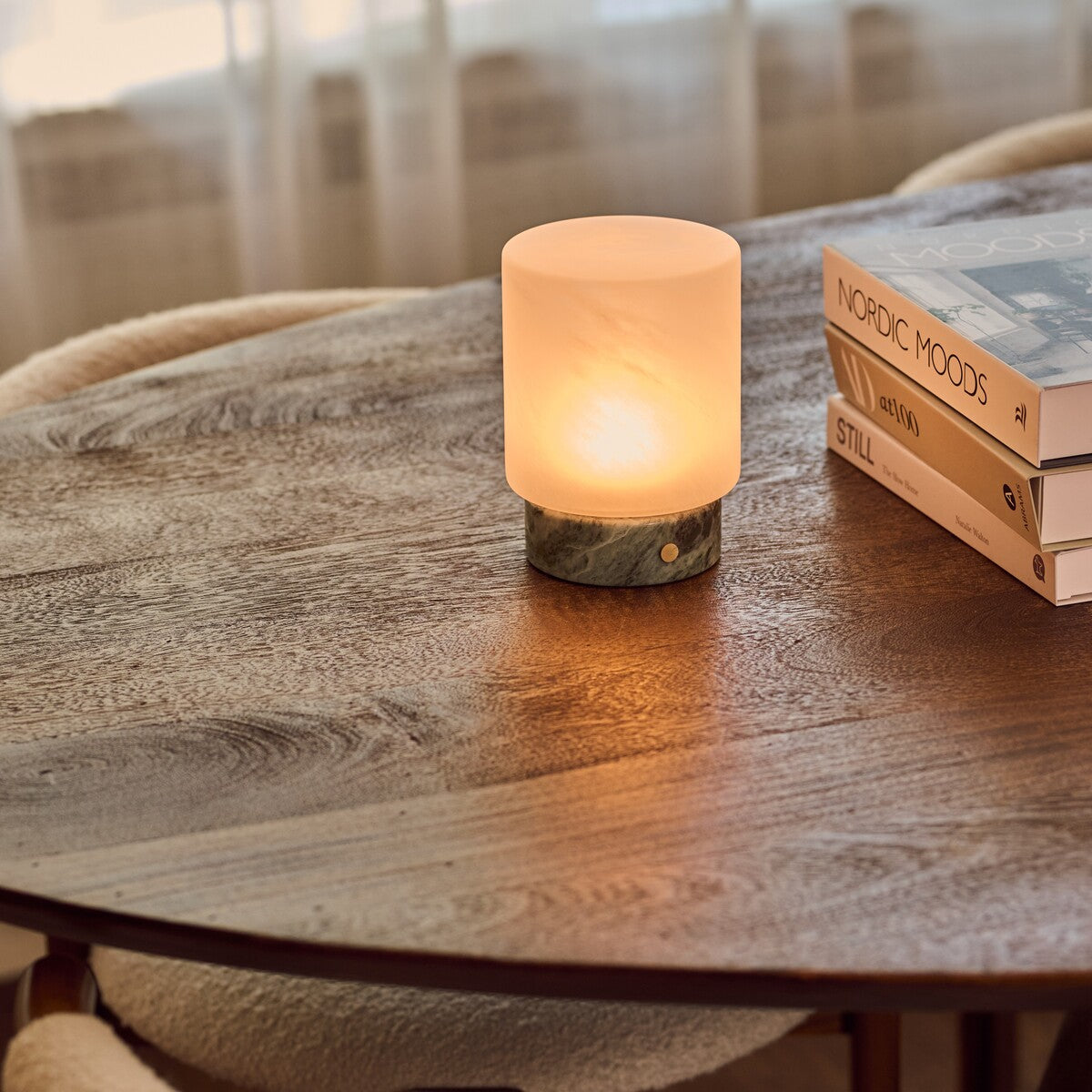 Cuyp Small cordless table lamp in Ice Green marble on a round wood table beside a stack of books