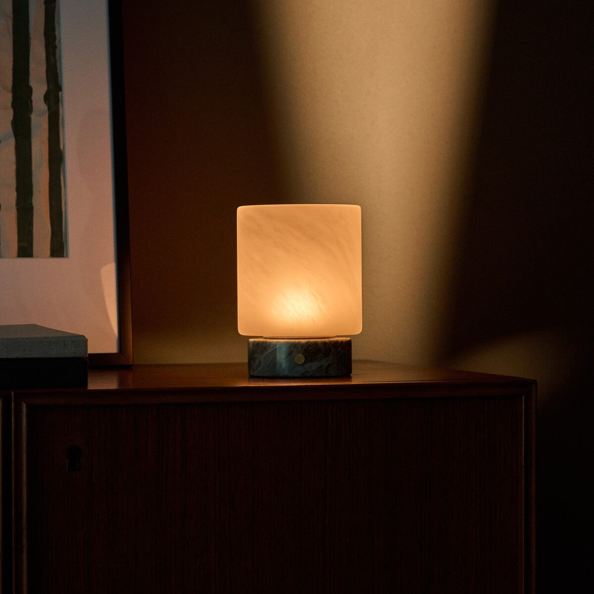 Tavellio Cuyp Small cordless table lamp in Ice Green marble casting a warm glow beside framed art