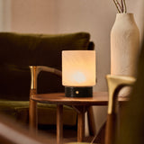Cuyp rechargeable table lamp in Nero Marquina marble glowing beside a green velvet sofa and ceramic vase