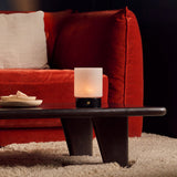 Cuyp cordless table lamp with black marble base glowing on a dark table beside a rust velvet sofa