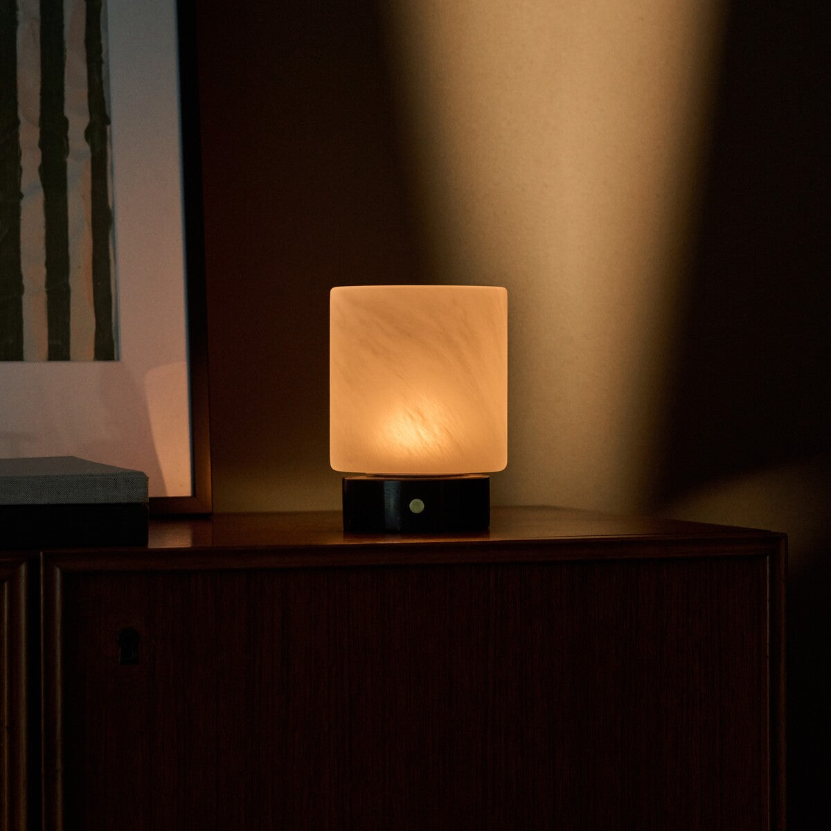 Tavellio Cuyp lamp with Nero Marquina marble base glowing warmly on a wooden sideboard at dusk