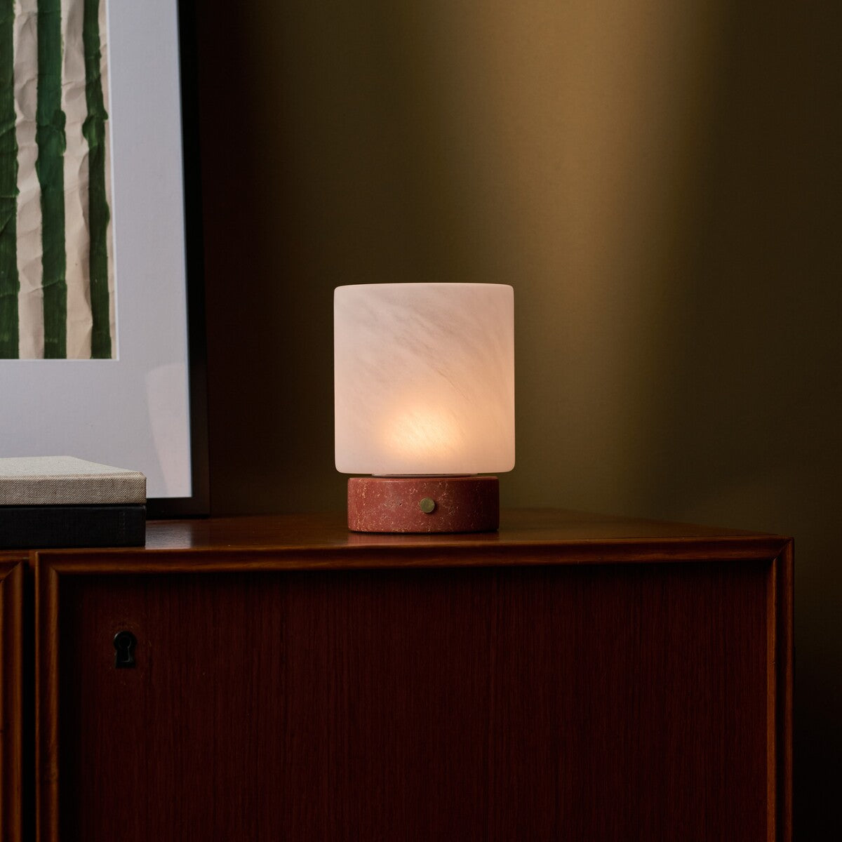 Lampe de table Cuyp Small travertin rouge rechargeable Tavellio - allumée sur un meuble ancien en bois dans une pièce sombre