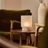 Cuyp Small Rosa Aurora lampe de table sans fil Tavellio – sur une table d'appoint en bois près d'un fauteuil vert velours et d'un vase