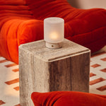 Cuyp Small Rosa Aurora lampe de table sans fil Tavellio – posée sur un cube en travertin près d'un canapé en velours côtelé orange