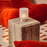 Cuyp Small Rosa Aurora lampe de table sans fil Tavellio – posée sur un cube en travertin près d'un canapé en velours côtelé orange