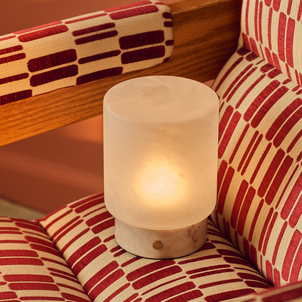Cuyp Small Rosa Aurora lampe de table sans fil Tavellio – nichée dans un fauteuil à motifs rouge et crème, ambiance chaleureuse