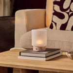 Cuyp Small Rosa Aurora lampe de table rechargeable Tavellio – posée sur une pile de livres près d'un fauteuil beige et coussin bordeaux