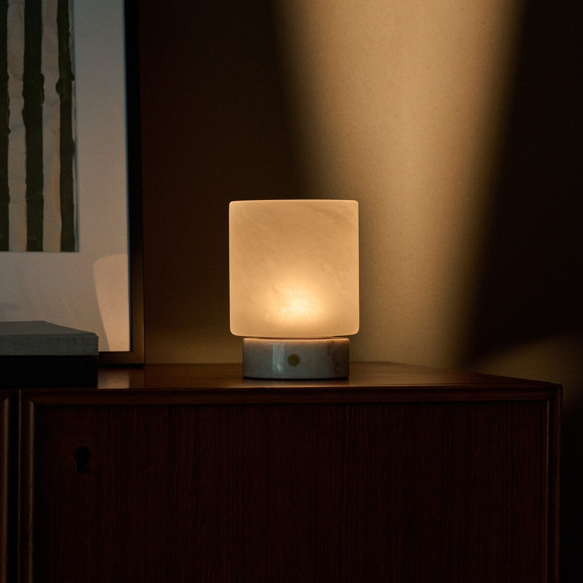 Cuyp Small Rosa Aurora lampe de table rechargeable Tavellio – sur un meuble en bois foncé près d'un cadre botanique, lumière du soir