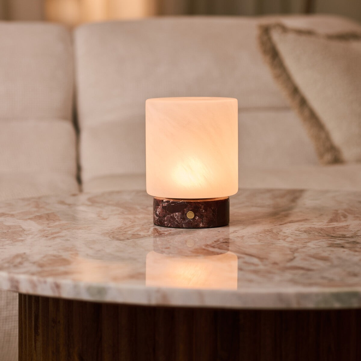 Cuyp rechargeable table lamp in Rosso Levanto marble reflected on a marble table beside a beige sofa