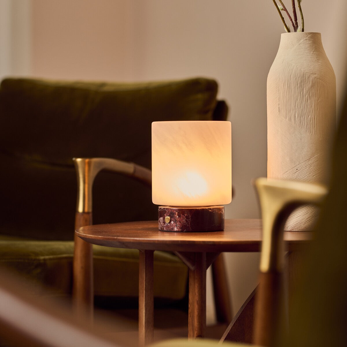 Cuyp rechargeable table lamp in Rosso Levanto marble glowing beside a green velvet sofa and vase