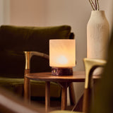 Cuyp rechargeable table lamp in Rosso Levanto marble glowing beside a green velvet sofa and vase