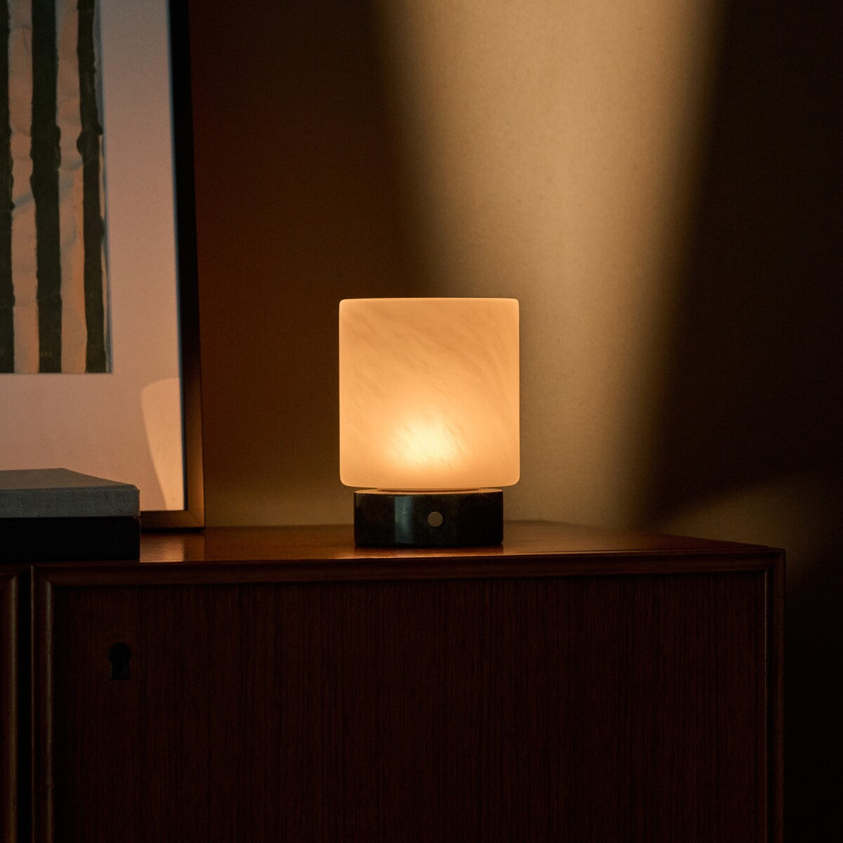 Tavellio Cuyp Small cordless table lamp in Verde Alpi marble lit beside striped wall art on a wood cabinet