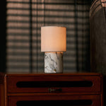 Dou cordless table lamp in Arabescato marble casting warm light on a nightstand in a dim bedroom