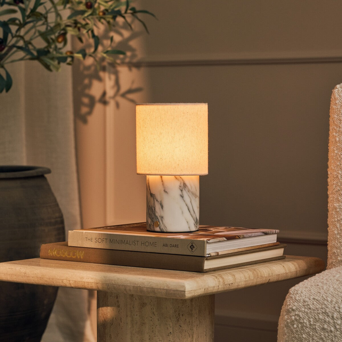 Dou cordless table lamp in Arabescato marble glowing beside stacked books and an olive branch