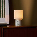 Dou Arabescato marble rechargeable table lamp lit on a wood sideboard beside a striped art print