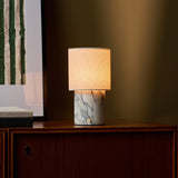 Dou Arabescato marble rechargeable table lamp lit on a wood sideboard beside a striped art print