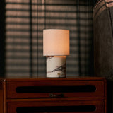 Dou Calacatta Vionaro lampe de table rechargeable Tavellio – sur une commode en bois – plaid à rayures roses posé à côté