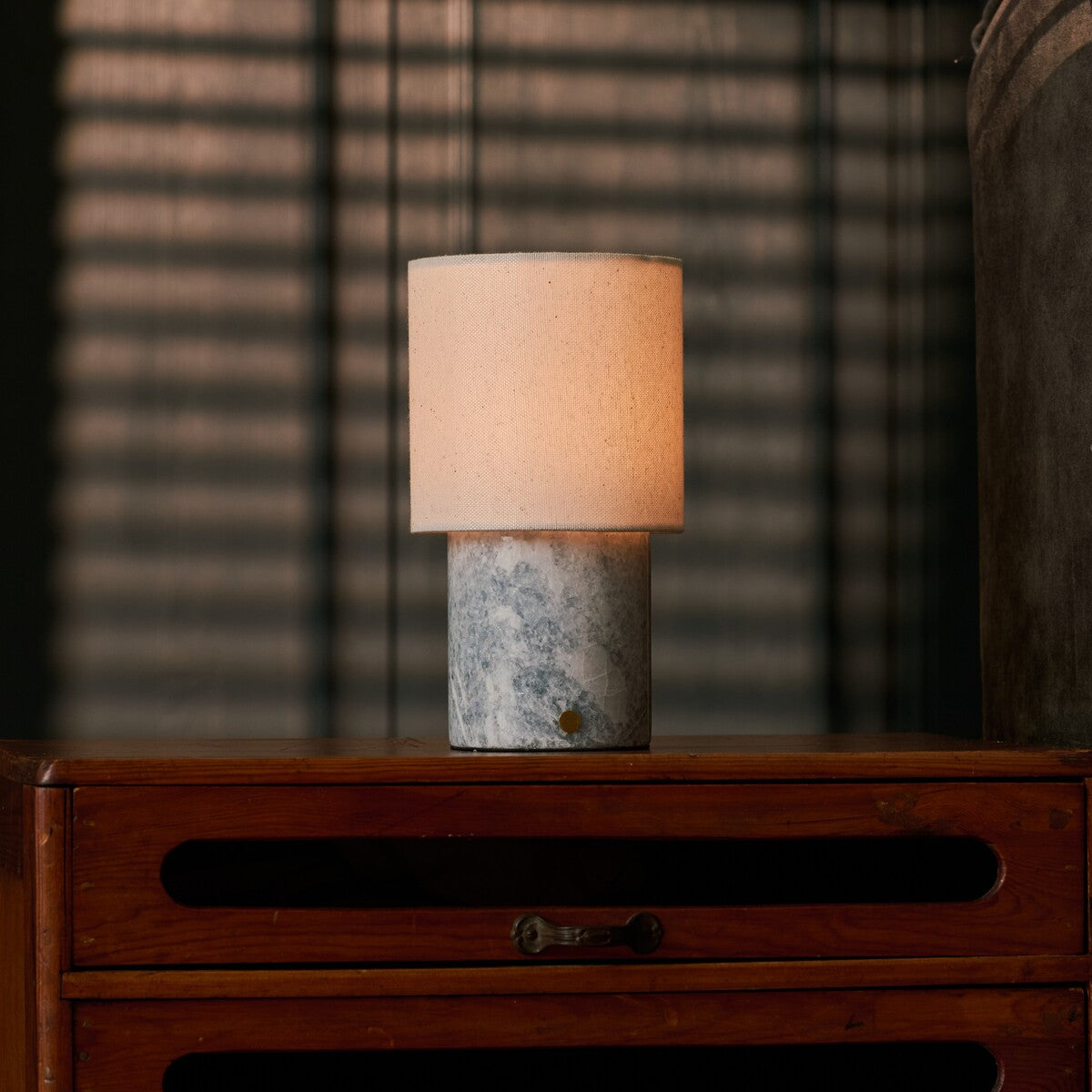 Tavellio Dou rechargeable table lamp beside a striped throw blanket on a wood dresser, Blue Calcite marble base