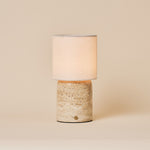 Cordless table lamp Dou Large Classic Travertine with a cream linen shade on a plain studio backdrop