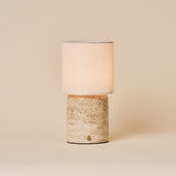 Cordless table lamp Dou Large Classic Travertine with a cream linen shade on a plain studio backdrop