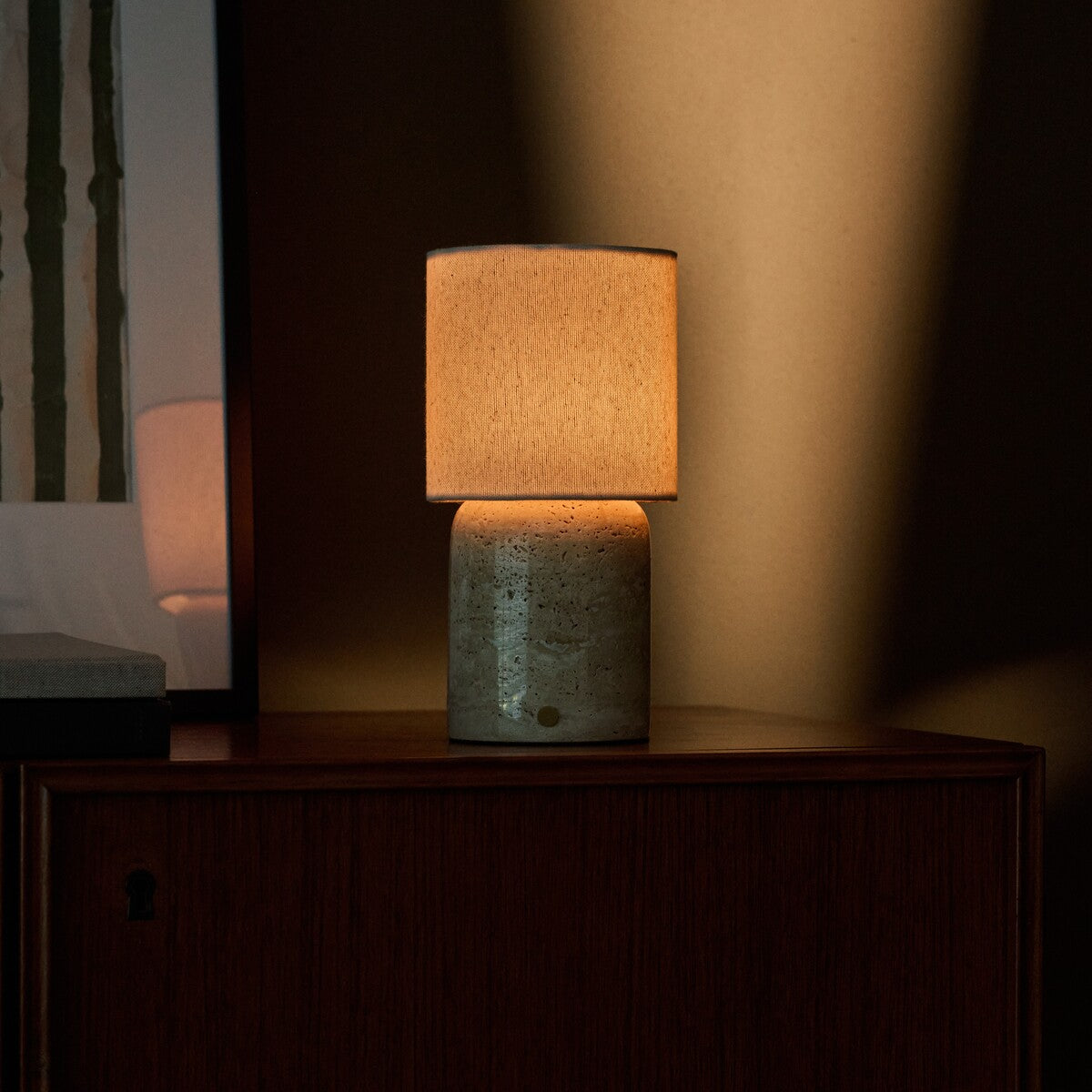 Tavellio Dou Large Classic Travertine table lamp casting warm light on a dark wood sideboard