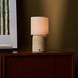 Rechargeable table lamp Dou Large Classic Travertine glowing beside a framed print on a wood cabinet