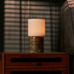 Dou Large rechargeable table lamp with linen shade glowing on a wood nightstand beside a striped pillow