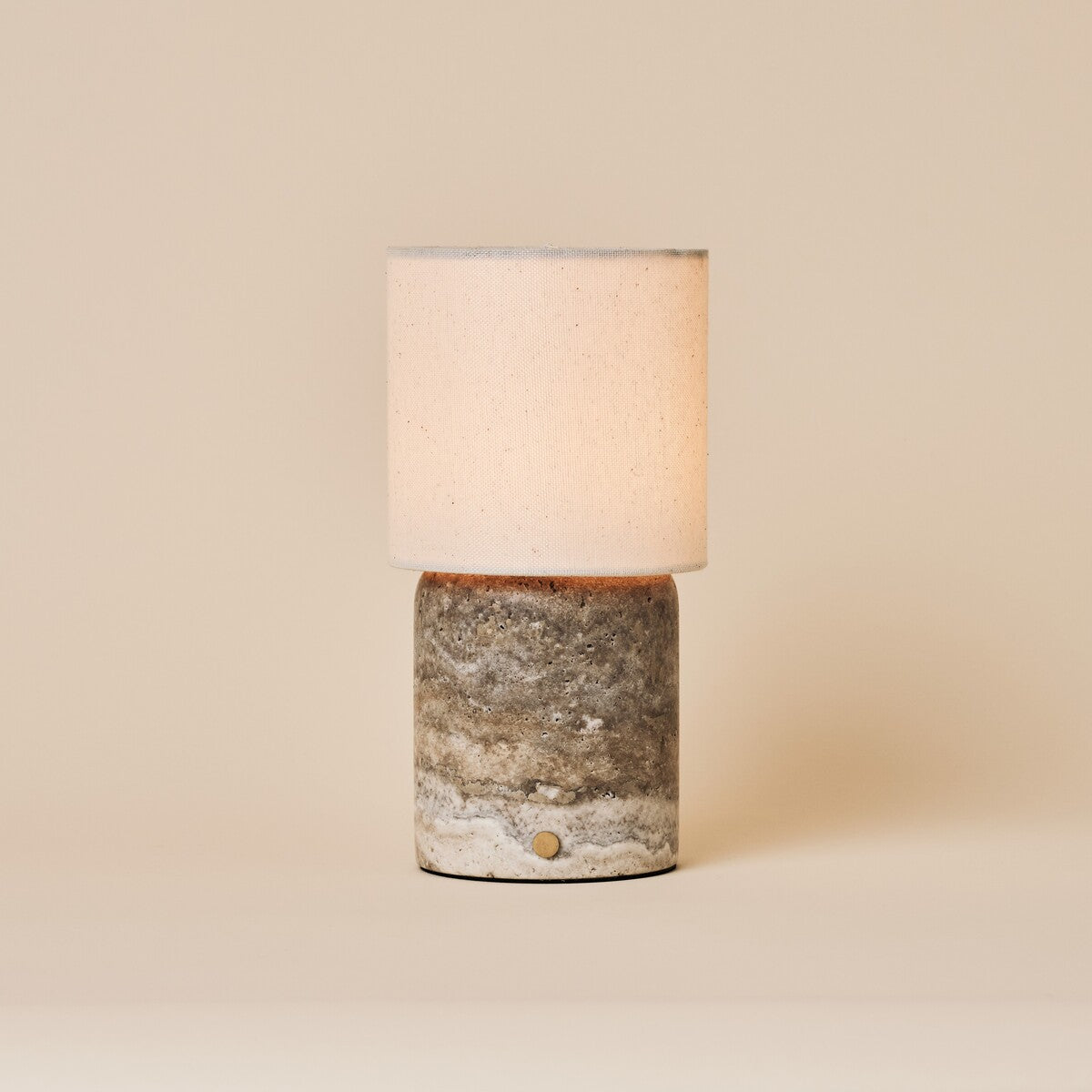 Rechargeable table lamp Dou Large Silver Travertine with a natural linen shade on a beige backdrop