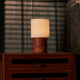 Dou Red Travertine rechargeable table lamp lit on a wood dresser beside slatted window blinds