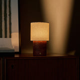Tavellio Dou cordless table lamp in red travertine casting warm light on a mid-century cabinet