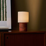 Dou Red Travertine rechargeable table lamp glowing on a wood sideboard against an olive wall