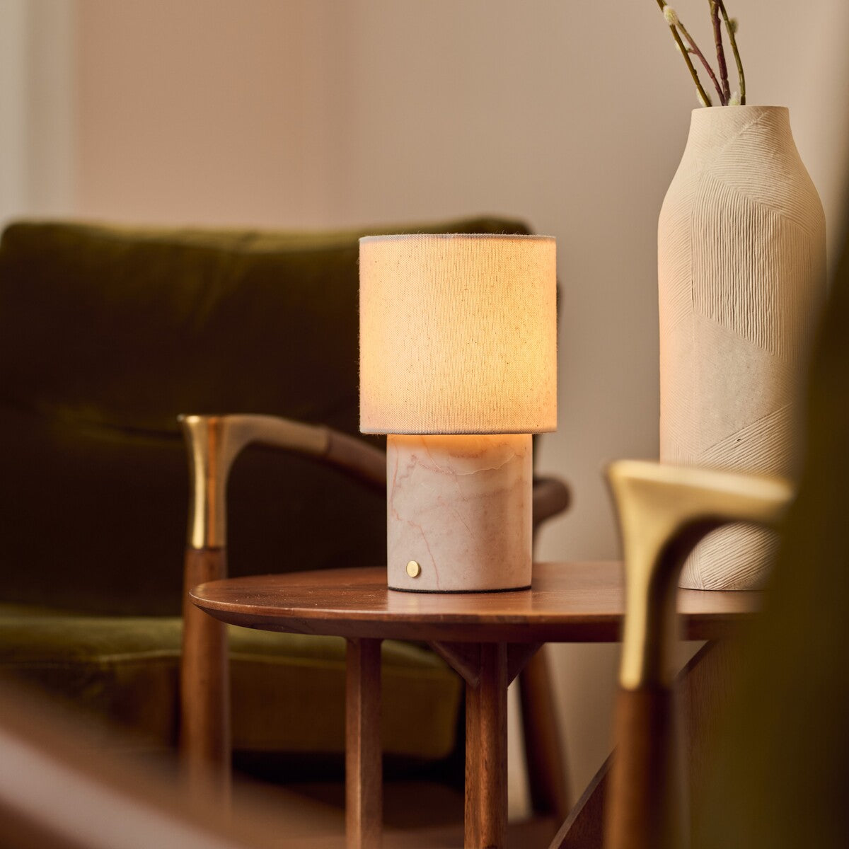 Dou Rosa Aurora lampe de table rechargeable Tavellio – posée sur une table d'appoint – canapé en velours vert et vase en céramique