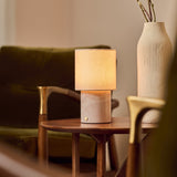 Dou Rosa Aurora lampe de table rechargeable Tavellio – posée sur une table d'appoint – canapé en velours vert et vase en céramique