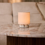 Cordless Dou Small Arabescato Marble Table Lamp glowing on a round marble coffee table beside a beige sofa