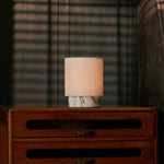 Cordless Dou Small Arabescato Marble Table Lamp glowing on a wooden dresser in front of striped blinds