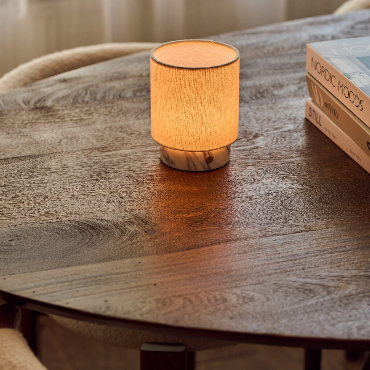 Dou Small Arabescato Marble Rechargeable Table Lamp lit on a wooden table next to a stack of design books