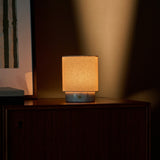 Cordless table lamp Dou Small in Bianco Statuarietto marble lit on a nightstand with striped blind-shadow light