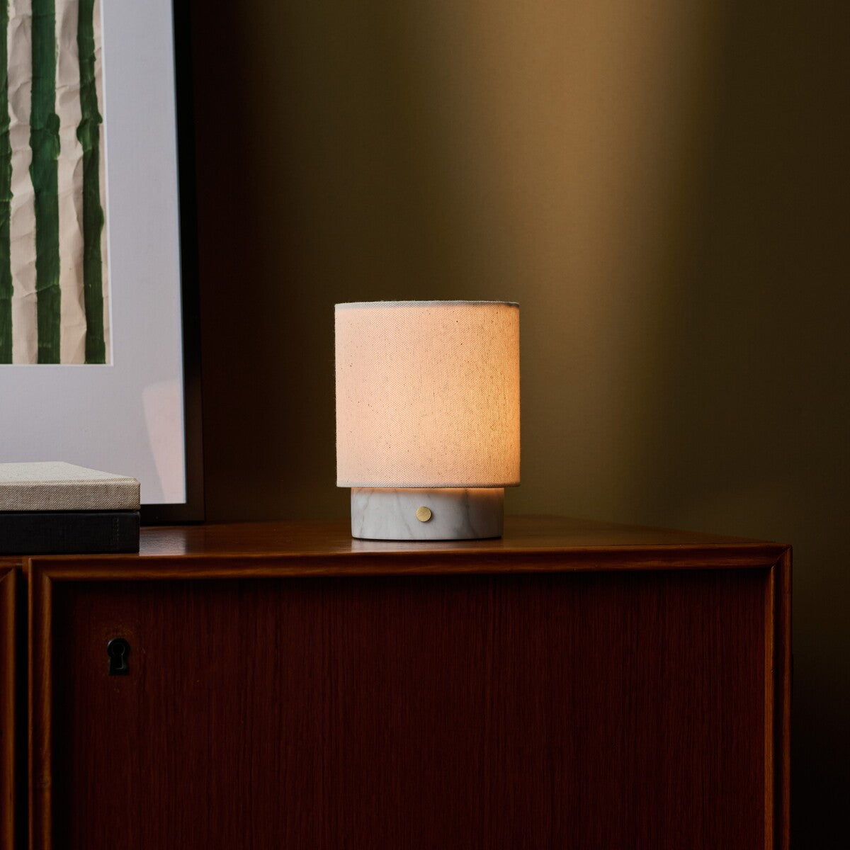 Dou Small rechargeable table lamp in Bianco Statuarietto marble glowing on a wood sideboard at night