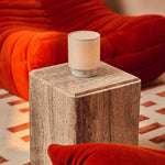 Cordless table lamp Dou Small, Bianco Statuarietto marble, styled on a travertine side table beside a red sofa