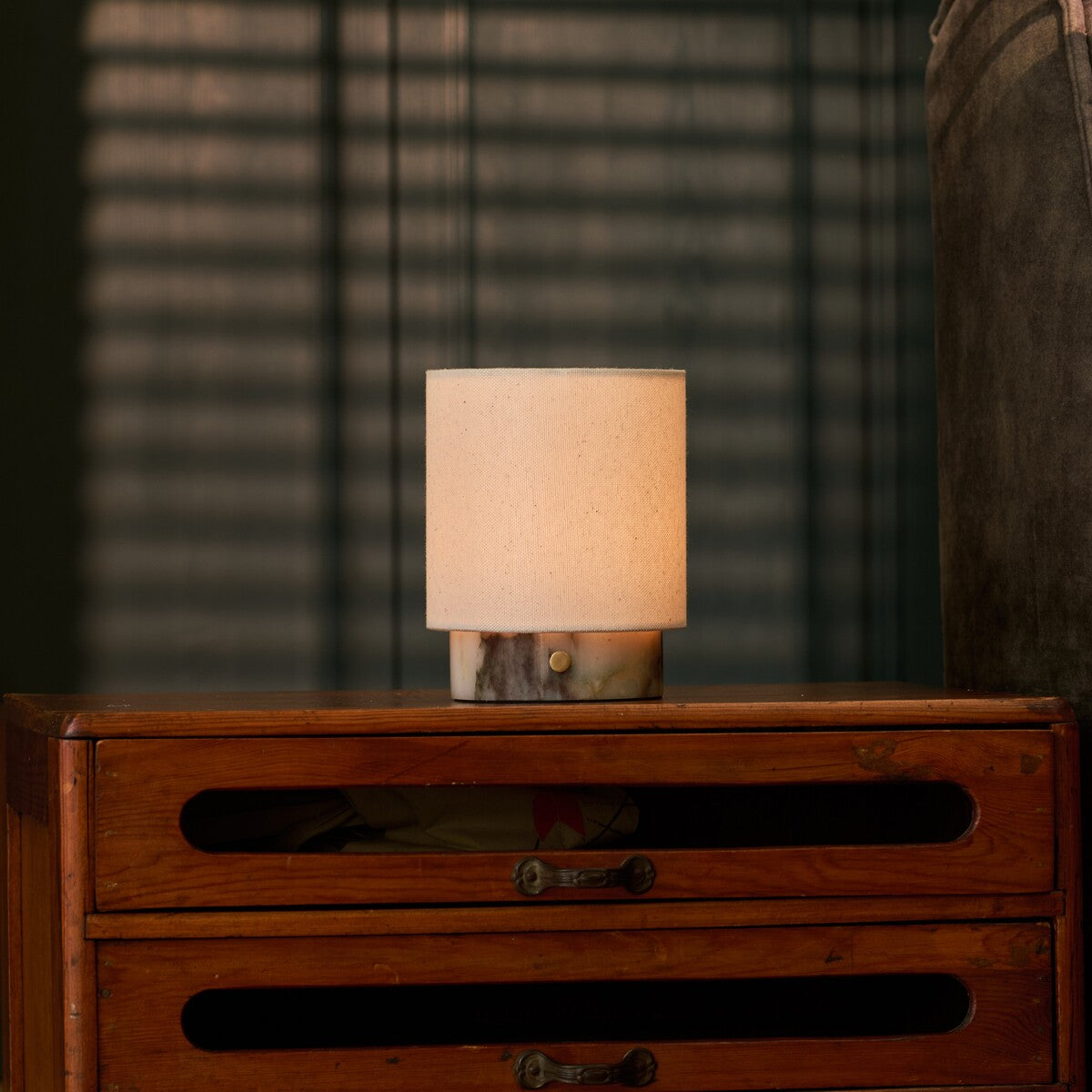 Dou Small rechargeable table lamp in Calacatta Viola marble glowing atop a vintage chest of drawers