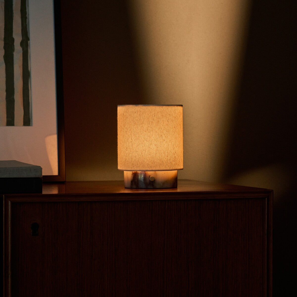 Cordless table lamp Dou Small in Calacatta Viola marble lit close-up on a wood sideboard at dusk