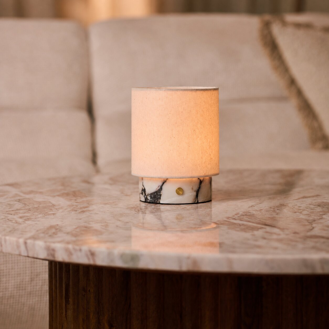 Dou Small cordless table lamp in white marble glowing on a coffee table beside a beige sofa